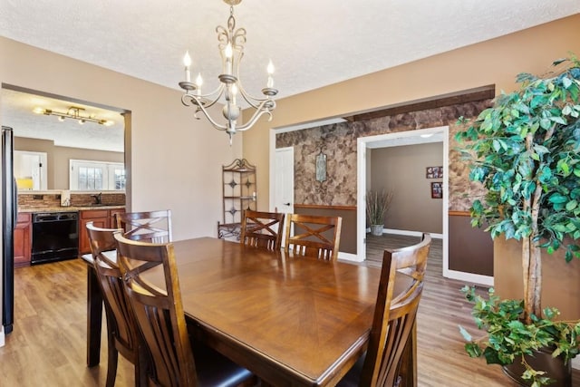 dining area with a chandelier, sink, a textured ceiling, and light wood-type flooring