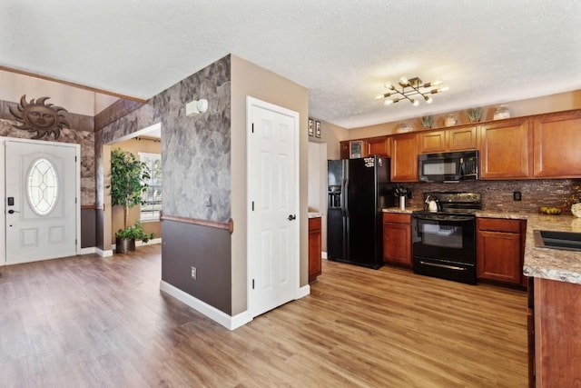 kitchen with decorative backsplash, black appliances, a textured ceiling, and light wood-type flooring