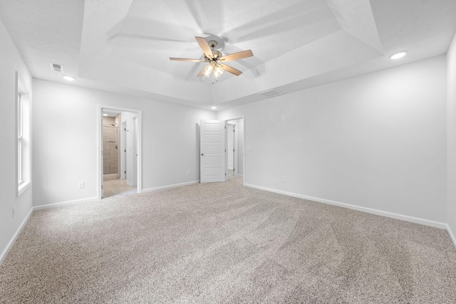 unfurnished bedroom featuring ceiling fan, connected bathroom, a tray ceiling, carpet floors, and a textured ceiling