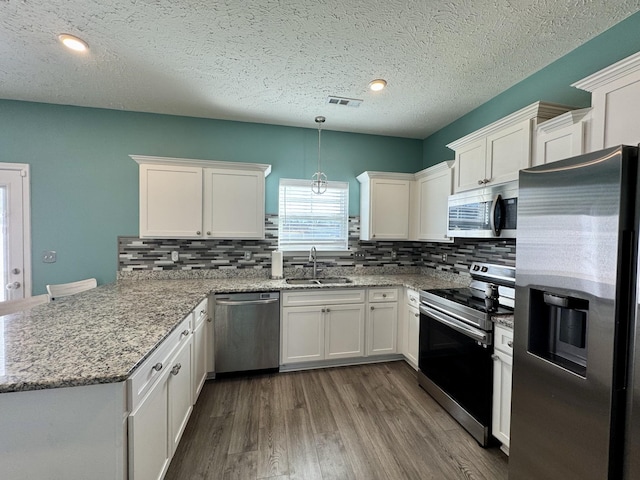 kitchen featuring appliances with stainless steel finishes, white cabinetry, wood-type flooring, sink, and hanging light fixtures