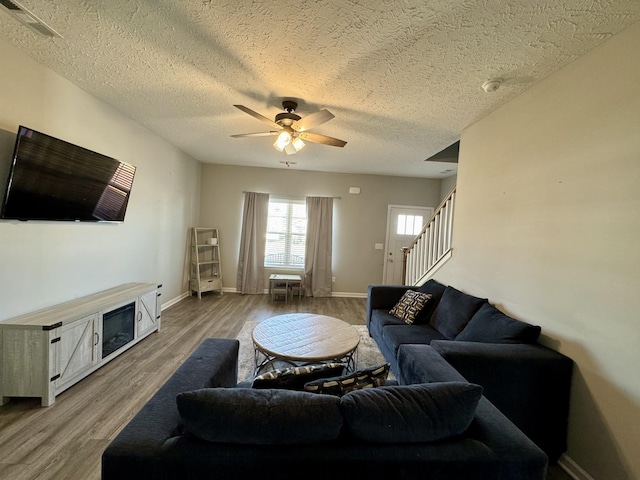 living room featuring ceiling fan, hardwood / wood-style floors, a textured ceiling, and a fireplace