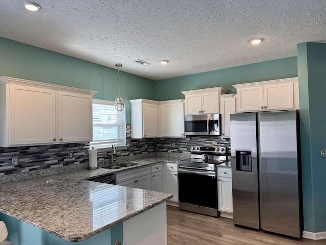 kitchen with white cabinetry, stainless steel appliances, kitchen peninsula, and dark stone counters