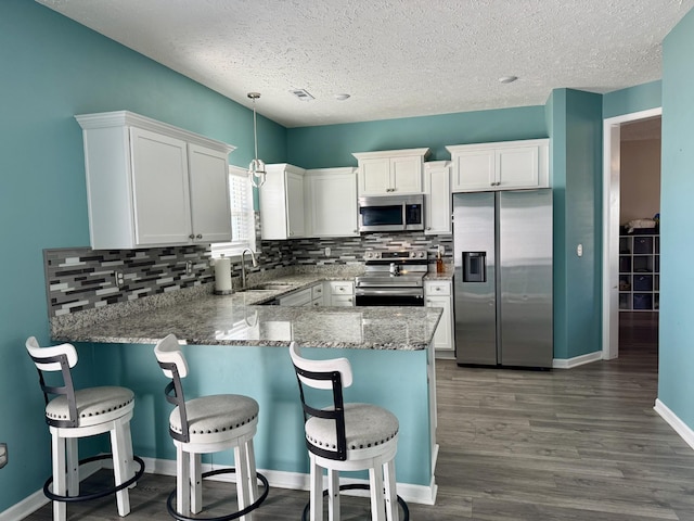 kitchen featuring sink, kitchen peninsula, pendant lighting, stainless steel appliances, and white cabinets