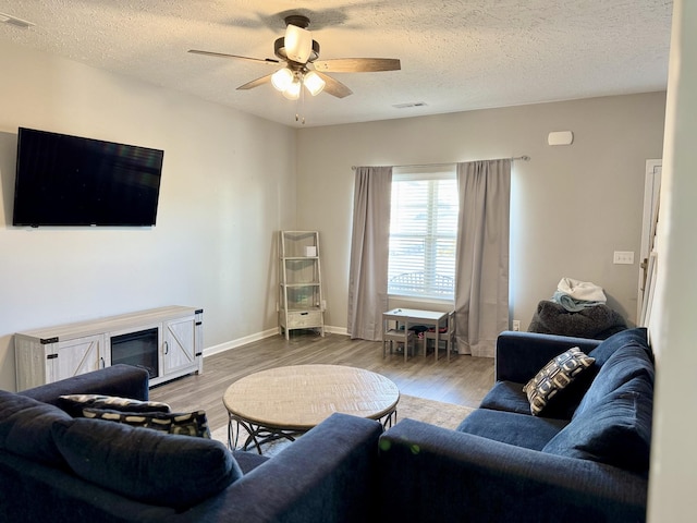 living room with a textured ceiling, a fireplace, ceiling fan, and light wood-type flooring