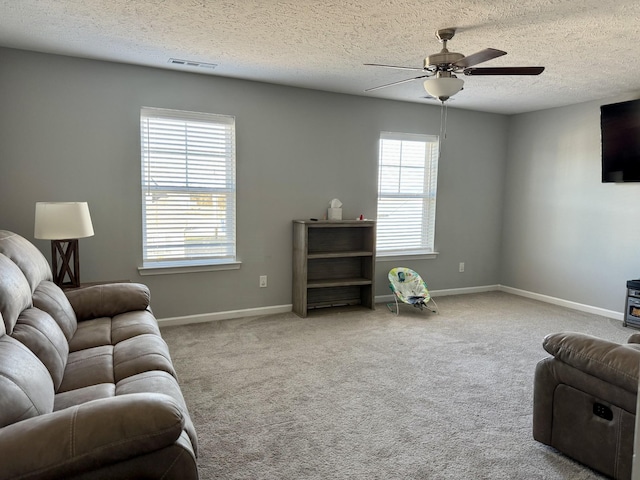 living room featuring a textured ceiling, light colored carpet, ceiling fan, and a wood stove