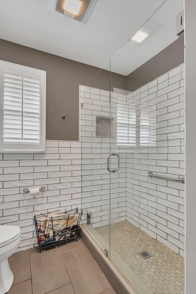 bathroom with tile walls, tile patterned floors, a shower with door, and toilet