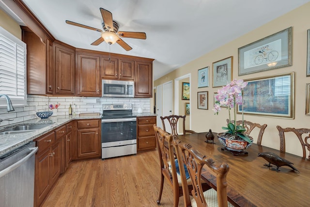 kitchen featuring sink, appliances with stainless steel finishes, light stone countertops, decorative backsplash, and light wood-type flooring