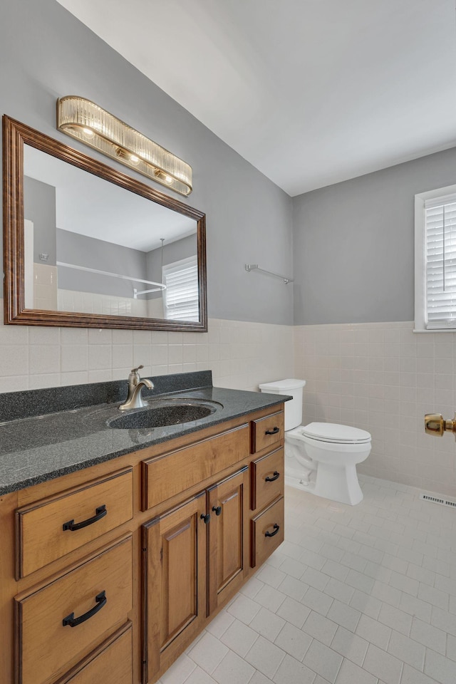 bathroom featuring a healthy amount of sunlight, vanity, toilet, and tile walls