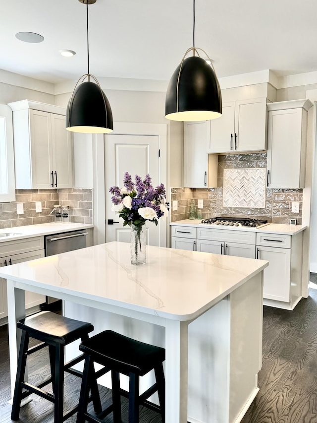 kitchen with hanging light fixtures, appliances with stainless steel finishes, a kitchen island, light stone countertops, and white cabinets