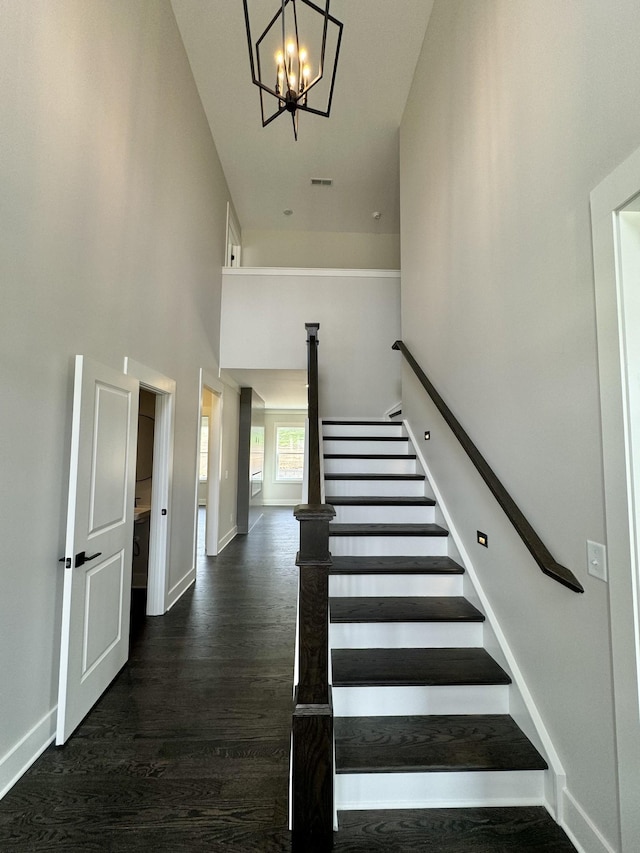 stairway with wood-type flooring, a chandelier, and a high ceiling