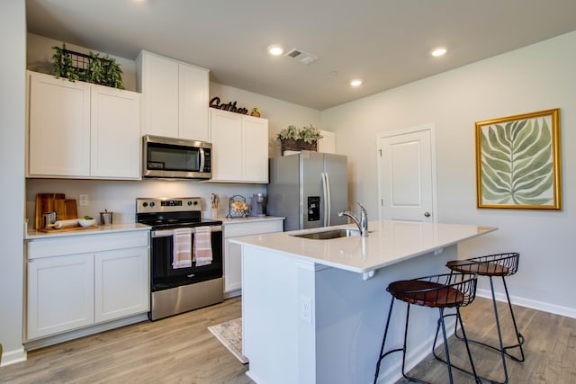 kitchen with sink, white cabinetry, appliances with stainless steel finishes, a kitchen island with sink, and light hardwood / wood-style floors