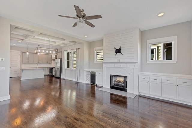 unfurnished living room featuring dark hardwood / wood-style floors, a fireplace, beamed ceiling, wine cooler, and coffered ceiling