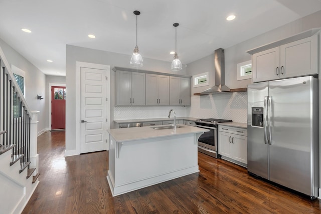 kitchen featuring pendant lighting, sink, stainless steel appliances, a center island with sink, and wall chimney range hood