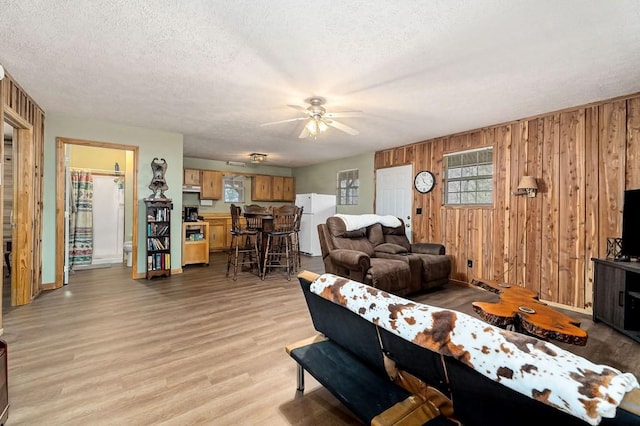 living room featuring plenty of natural light, wooden walls, a textured ceiling, and light hardwood / wood-style floors