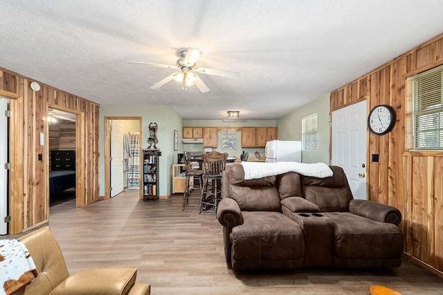 living room with ceiling fan, a textured ceiling, light wood-type flooring, and wood walls