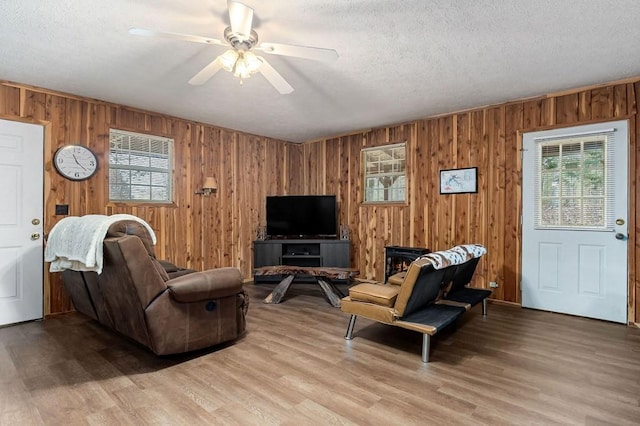 living room with ceiling fan, wood walls, light hardwood / wood-style flooring, and a textured ceiling