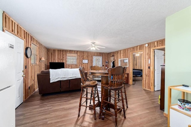 dining space with dark hardwood / wood-style flooring, ceiling fan, a textured ceiling, and wood walls