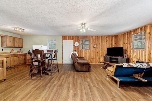 living room with ceiling fan, wooden walls, a textured ceiling, and light wood-type flooring