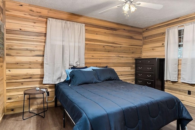 bedroom with ceiling fan, hardwood / wood-style flooring, wooden walls, and a textured ceiling