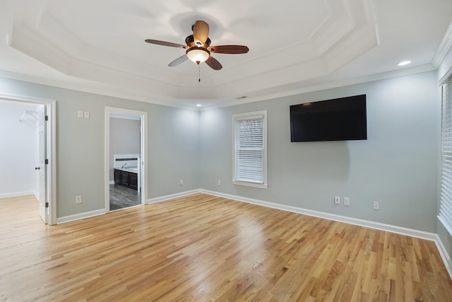 interior space with ensuite bathroom, a spacious closet, ornamental molding, a tray ceiling, and light hardwood / wood-style floors