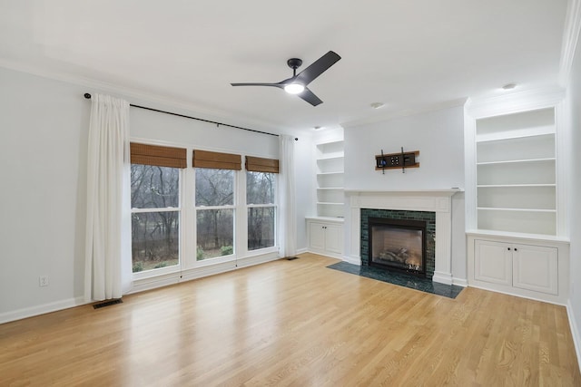 unfurnished living room with crown molding, ceiling fan, built in features, and light hardwood / wood-style floors