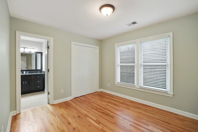 unfurnished bedroom featuring multiple windows, connected bathroom, light hardwood / wood-style floors, and a closet