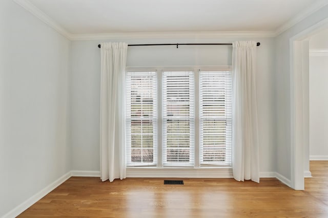 spare room with crown molding, plenty of natural light, and light hardwood / wood-style floors