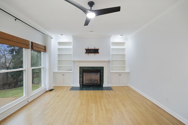 unfurnished living room featuring a tile fireplace, light hardwood / wood-style flooring, ceiling fan, crown molding, and built in shelves