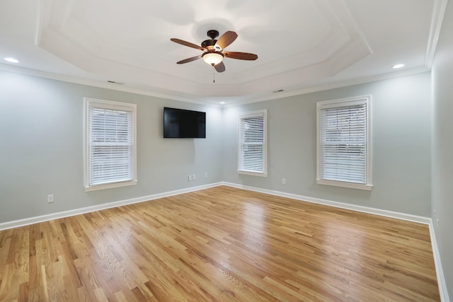 empty room with a raised ceiling, crown molding, ceiling fan, and light hardwood / wood-style floors