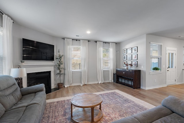 living area featuring light wood-style floors, a fireplace with flush hearth, visible vents, and baseboards