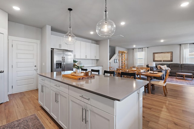 kitchen featuring stainless steel fridge, hanging light fixtures, a center island, light hardwood / wood-style floors, and white cabinets