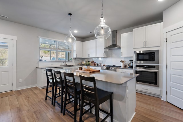 kitchen featuring a breakfast bar area, stainless steel appliances, white cabinets, a center island, and wall chimney exhaust hood