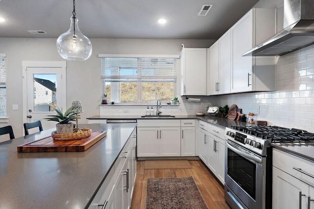 kitchen with dark countertops, wall chimney range hood, stainless steel gas range oven, and white cabinetry