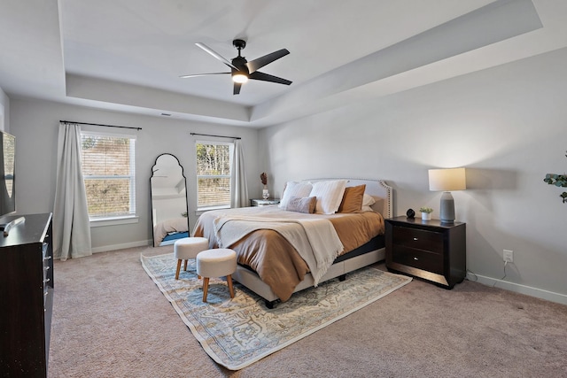 bedroom featuring a ceiling fan, a tray ceiling, light colored carpet, and baseboards