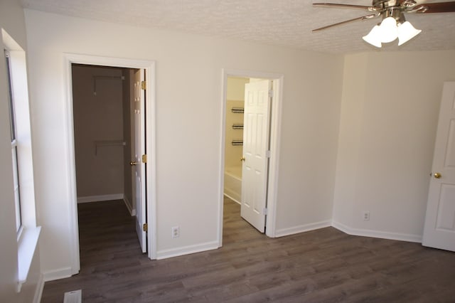 unfurnished bedroom with a closet, a spacious closet, dark hardwood / wood-style floors, and a textured ceiling