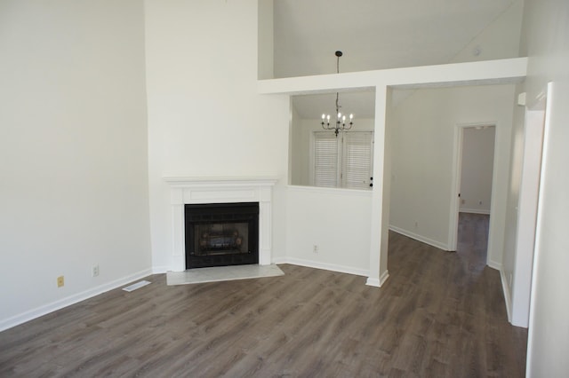 unfurnished living room featuring an inviting chandelier, a towering ceiling, and dark hardwood / wood-style floors