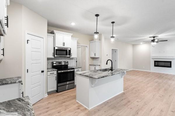 kitchen featuring sink, appliances with stainless steel finishes, an island with sink, pendant lighting, and white cabinets