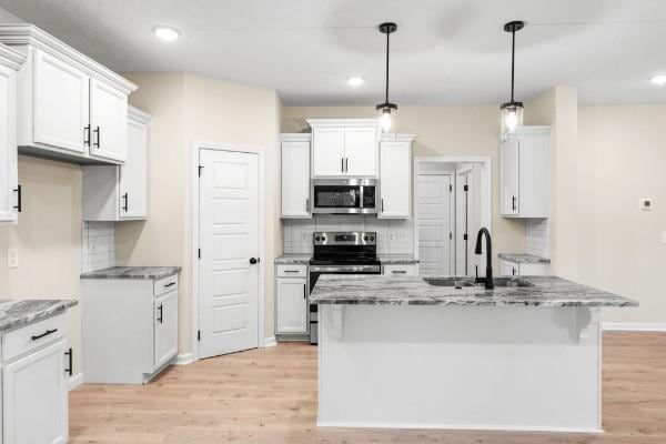 kitchen with pendant lighting, stainless steel appliances, light stone countertops, and white cabinets