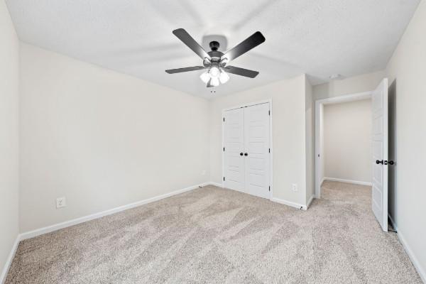 unfurnished bedroom with ceiling fan, light colored carpet, and a closet