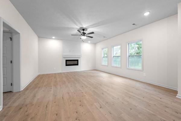 unfurnished living room featuring ceiling fan, a large fireplace, and light hardwood / wood-style flooring