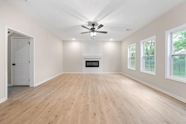 unfurnished living room featuring a large fireplace, ceiling fan, and light hardwood / wood-style flooring