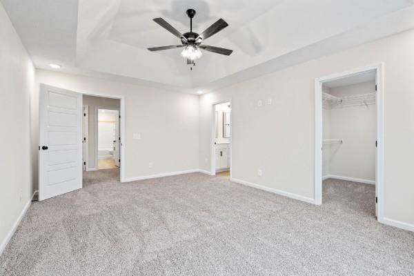 unfurnished bedroom with ceiling fan, a tray ceiling, light carpet, a walk in closet, and a closet