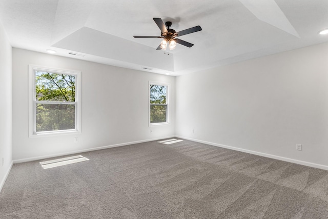 empty room featuring a tray ceiling, ceiling fan, and carpet flooring