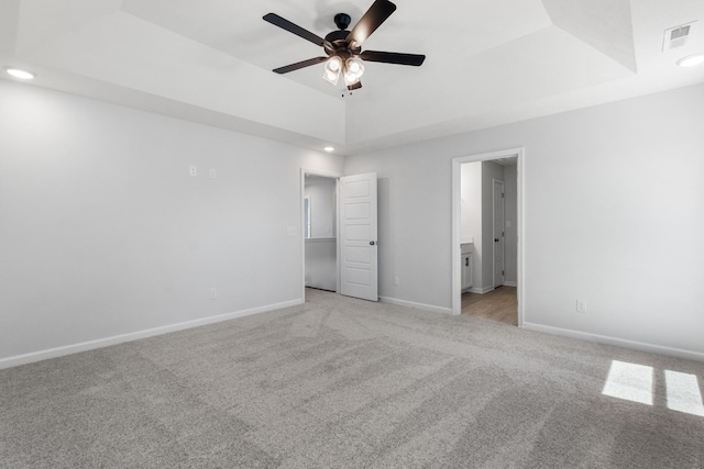 unfurnished bedroom featuring ceiling fan, ensuite bathroom, a raised ceiling, and light carpet