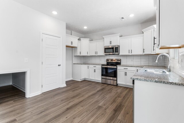 kitchen with appliances with stainless steel finishes, white cabinetry, sink, light stone counters, and dark wood-type flooring