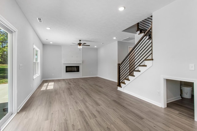 unfurnished living room featuring hardwood / wood-style flooring, a large fireplace, and ceiling fan