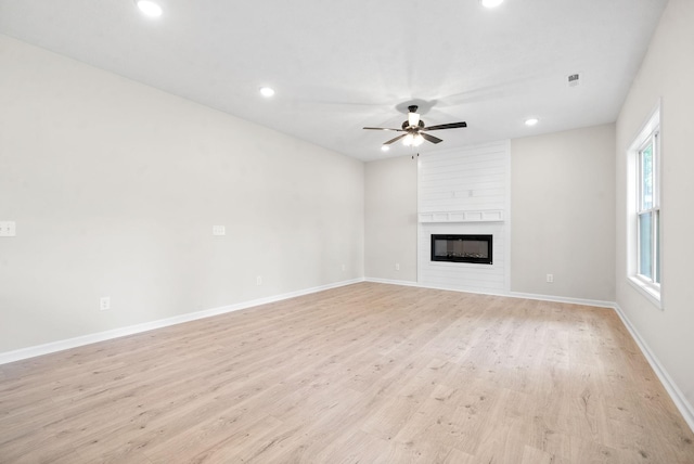 unfurnished living room with ceiling fan, a large fireplace, and light hardwood / wood-style floors