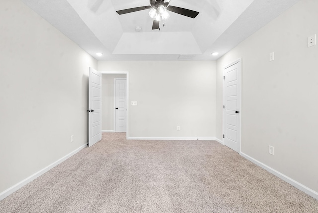 empty room featuring light carpet, a tray ceiling, and ceiling fan