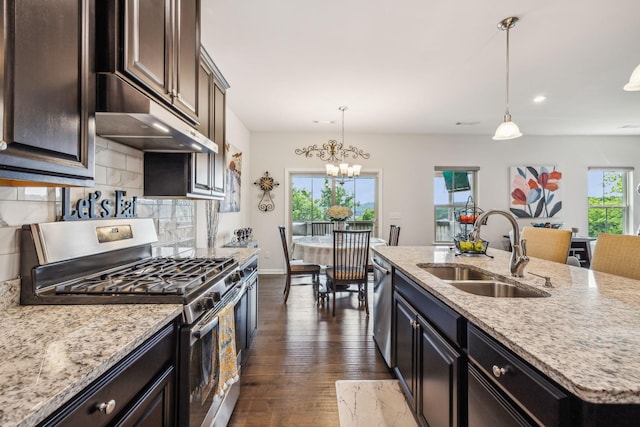 kitchen with stainless steel appliances, hanging light fixtures, sink, and a kitchen island with sink