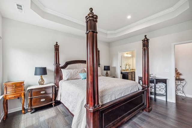 bedroom with a tray ceiling, dark wood-type flooring, ornamental molding, and ensuite bathroom